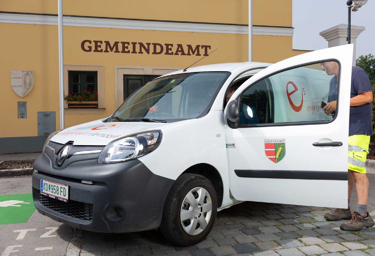 Das Foto zeigt ein E-Gemeindefahrzeug der Gemeinde Sierndorf, vor dem Gemeindeamt mit zwei Gemeindebediensteten.