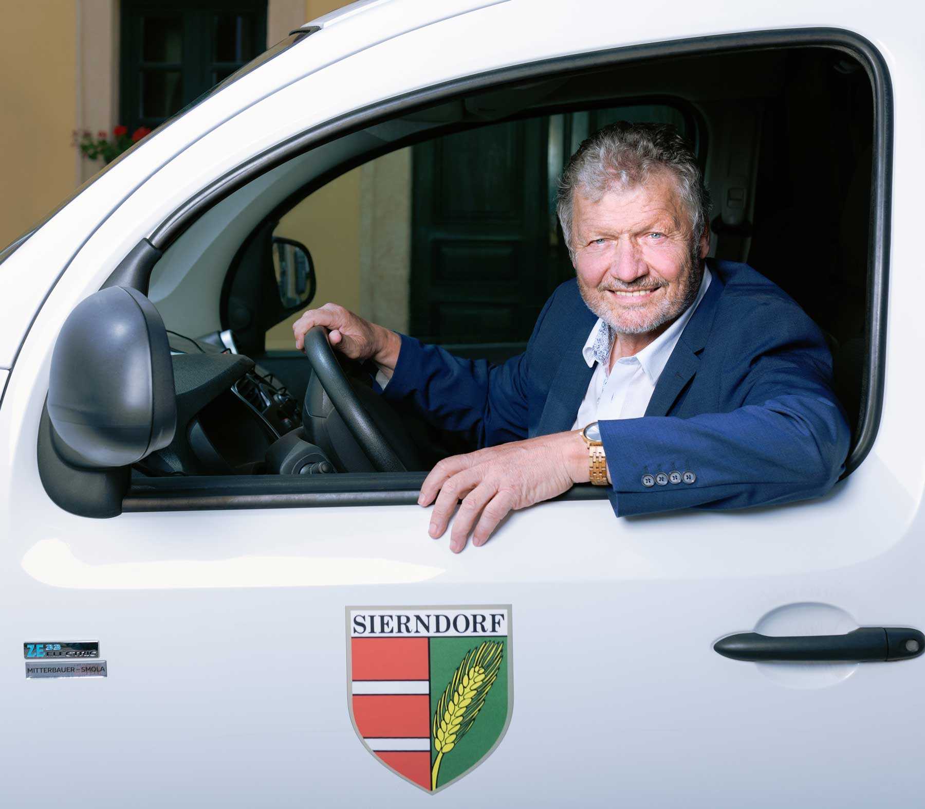 Das Foto zeigt einen lachenden Bürgermeister Muck aus seinem e - Gemeindefahrzeug schauend.